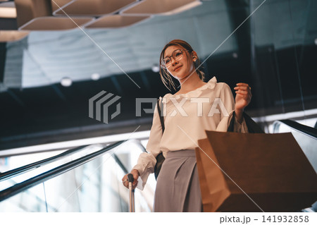 Young adult business woman holding shopping bags standing on escalator. 141932858
