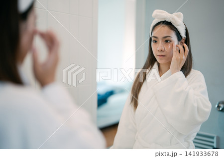 Asian woman in a bathrobe applying a eye facial sheet mask in bathroom skincare morning routine Asian woman in a bathrobe applying a eye facial sheet mask in bathroom skincare morning routine 141933678
