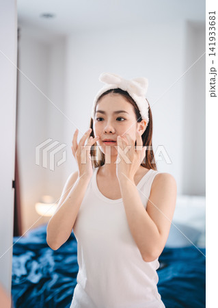 Asian woman applying a eye facial sheet mask in bedroom skincare and wellness morning routine Asian woman applying a eye facial sheet mask in bedroom skincare and wellness morning routine 141933681