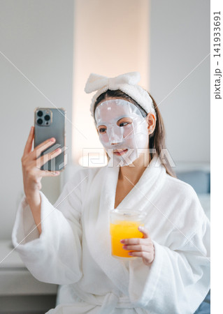 woman taking a selfie by mobile phone with a cosmetic mask on her face woman taking a selfie by mobile phone with a cosmetic mask on her face 141933691