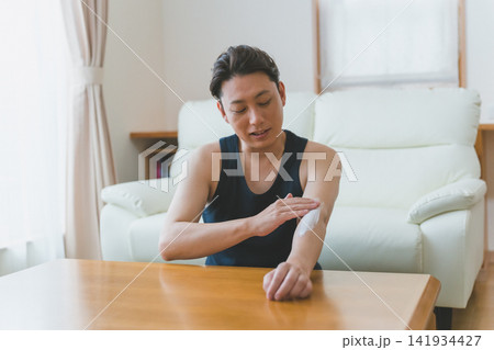 リビングで腕にクリームを塗り込む40代男性のメンズスキンケア 141934427
