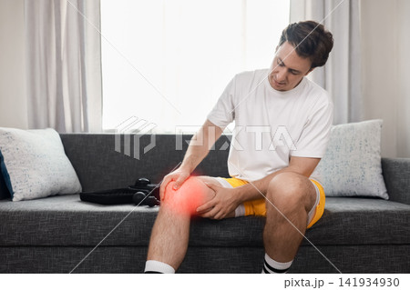 man holds his knee experiencing joint ache and pain from a sport injury, seeking therapy and recovery with a massager. 141934930