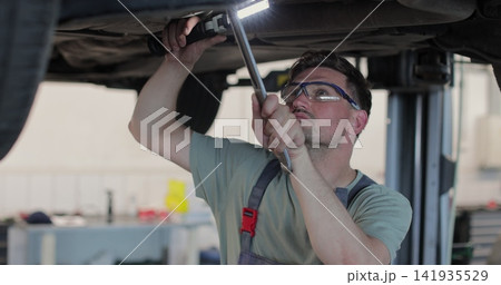Auto mechanic working underneath car lifting machine at the garage. Car auto service. 141935529