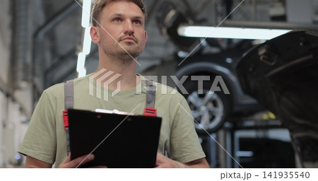Mechanic man with clipboard walking along workshop. Car service, repair, maintenance and people. Mechanic man with clipboard walking along workshop. Car service, repair, maintenance and people. 141935540