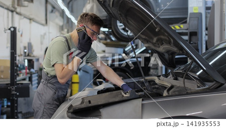 Mechanic talking on a mobile phone with the car owner while repairing a car in a garage. Mechanic talking on a mobile phone with the car owner while repairing a car in a garage. 141935553