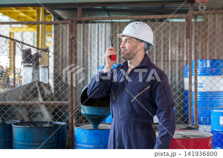 Construction worker communicating with radio at industrial site for safety. Construction worker communicating with radio at industrial site for safety. 141936800