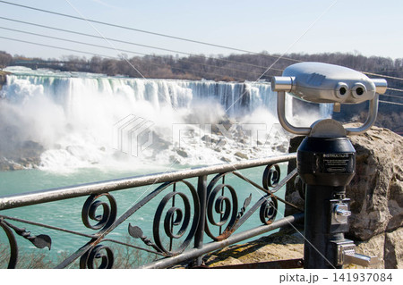 A closeup of coin operated viewing binoculars pointing at the Canadian Horseshoe Falls out of focus in the distance. Observation binoculars close-up with a view of the river and the city. High quality A closeup of coin operated viewing binoculars pointing at the Canadian Horseshoe Falls out of focus in the distance. Observation binoculars close-up with a view of the river and the city. High quality 141937084
