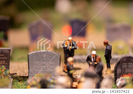 Miniature funeral mourners gathering among gravestones in a shallow depth cemetery scene Miniature funeral mourners gathering among gravestones in a shallow depth cemetery scene 141937422