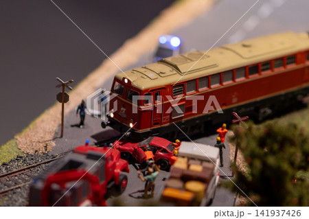 Miniature red locomotive collides with car at model railway crossing scene 141937426