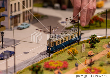 Adult hand adjusting miniature tram on detailed urban model railway layout Adult hand adjusting miniature tram on detailed urban model railway layout 141937439