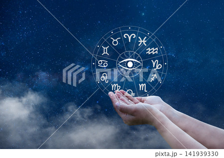 Cupped hands holding an astrology zodiac wheel with all seeing eye, under a starry Milky Way sky. 141939330