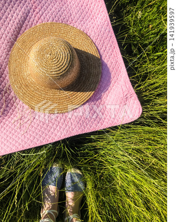 Summer flat lay. Picnic blanket, hat, woman legs on green grass. Summer flat lay. Picnic blanket, hat, woman legs on green grass. 141939597
