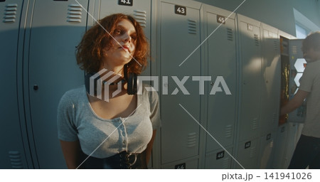 Creative Teen Girl Lost in Thoughts With Calm, Slightly Distant Gaze in School Locker Room Creative Teen Girl Lost in Thoughts With Calm, Slightly Distant Gaze in School Locker Room 141941026