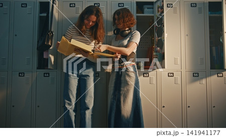 Two Teenage Girls Reviewing Homework Project by School Lockers 141941177