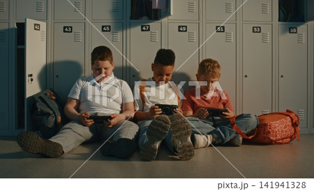 School Children Relax by Lockers While Sharing Content on Portable Devices Between Classes 141941328