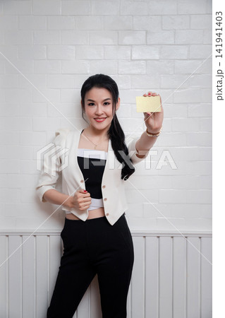 Fashion, shopping, banking and payment concept. Smiling beautiful Asian woman presenting credit card in hand on white wall. Fashion, shopping, banking and payment concept. Smiling beautiful Asian woman presenting credit card in hand on white wall. 141941403