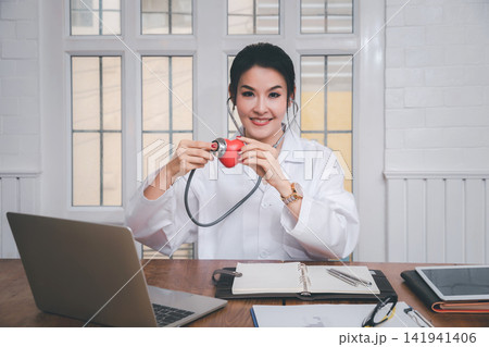 Professional female medical doctor holding a stethoscope check up on a red heart ball in office in the hospital. Concept of health care and medical. 141941406
