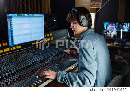 Sound engineer carefully calibrating sound levels in dimly lit studio Sound engineer carefully calibrating sound levels in dimly lit studio 141941955