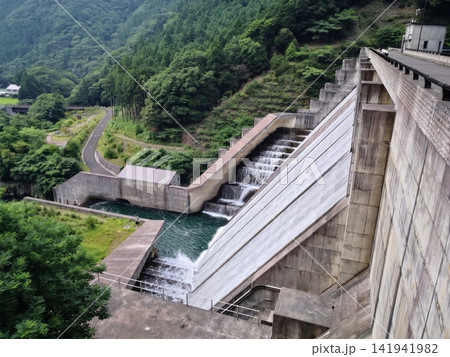 緑深い山間にあるダムの放流設備と流れ落ちる水 141941982