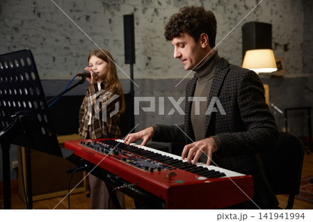 Caucasian coach accompanies girl vocalist at mic during focused studio rehearsal Caucasian coach accompanies girl vocalist at mic during focused studio rehearsal 141941994