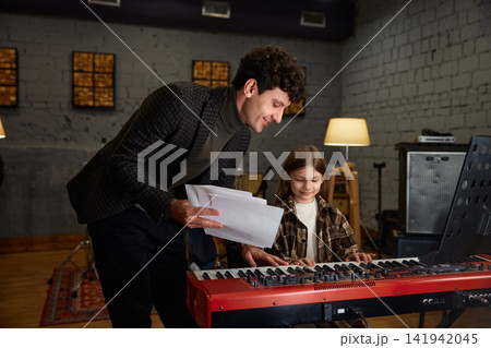Enthusiastic young girl practicing piano alongside her mentor in cozy studio setting 141942045
