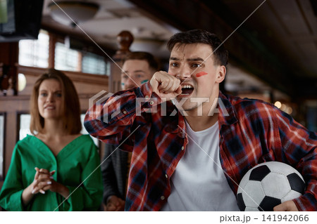 Man passionately celebrates goal in bustling pub filled with friends and excitement Man passionately celebrates goal in bustling pub filled with friends and excitement 141942066