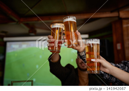 Friends toast as game plays. Attendees clink glasses while broadcast shows players on screen 141942087