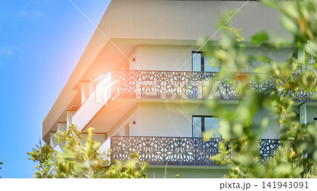 Modern residential building with new apartments in a green residential area. Eco architecture. Green tree and new apartment building. The harmony of nature and modernity. Modern residential building with new apartments in a green residential area. Eco architecture. Green tree and new apartment building. The harmony of nature and modernity. 141943091