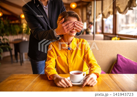 Man covering woman's eyes at a restaurant table Man covering woman's eyes at a restaurant table 141943723
