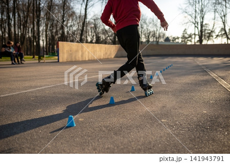 Young man in a red hoodie practicing freestyle rollerblading tricks Young man in a red hoodie practicing freestyle rollerblading tricks 141943791