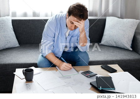 Stressed man calculating high utility bills at home. Rising energy prices, inflation, and economic crisis cause financial problems and economic pressure. Stressed man calculating high utility bills at home. Rising energy prices, inflation, and economic crisis cause financial problems and economic pressure. 141943813