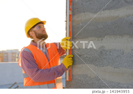 Construction worker using spirit level on building site at sunset Construction worker using spirit level on building site at sunset 141943955