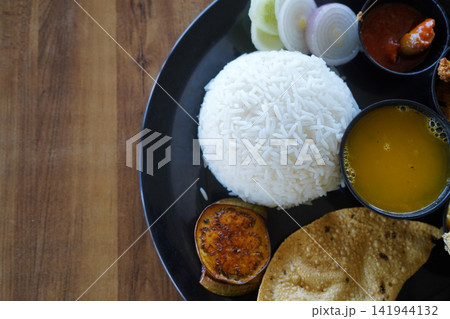 Traditional Indian Bengali meal platter served with steamed rice dal papad fried eggplant salad and side dishes on a black plate Traditional Indian Bengali meal platter served with steamed rice dal papad fried eggplant salad and side dishes on a black plate 141944132