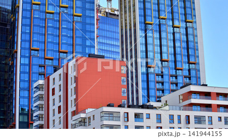 A low-rise residential building stands against a backdrop of tall glass buildings. An urban quarter of modern architecture. 141944155