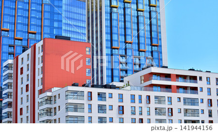 A low-rise residential building stands against a backdrop of tall glass buildings. An urban quarter of modern architecture. 141944156