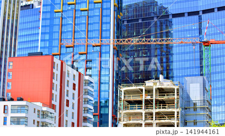 A low-rise residential building stands against a backdrop of tall glass buildings. An urban quarter of modern architecture. A low-rise residential building stands against a backdrop of tall glass buildings. An urban quarter of modern architecture. 141944161