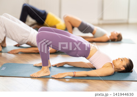 Asian woman performs glute bridge during Pilates multinational training Asian woman performs glute bridge during Pilates multinational training 141944630