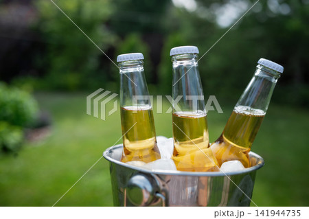 Close up of cold bottled beer in ice bucket on sunny summer backyard Close up of cold bottled beer in ice bucket on sunny summer backyard 141944735