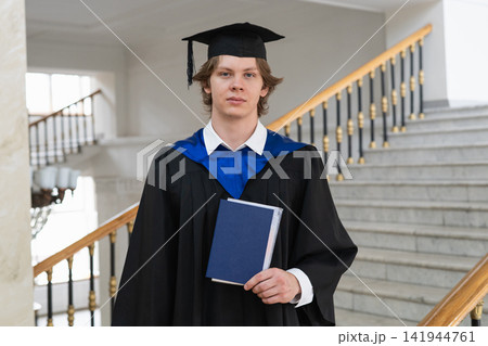 Young university graduate holding diploma folder on campus staircase Young university graduate holding diploma folder on campus staircase 141944761