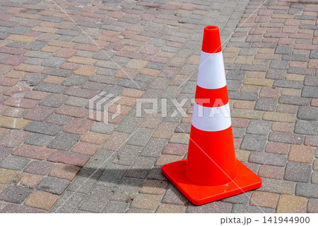 Bright Orange Traffic Safety Cone with Reflective White Stripes on a Paved Pedestrian Street Surface Bright Orange Traffic Safety Cone with Reflective White Stripes on a Paved Pedestrian Street Surface 141944900