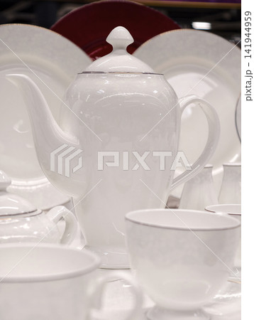 White porcelain cups on saucers tall minimalist teapot and plates behind arranged as premium kitchenware set in refined retail presentation for store shelf display White porcelain cups on saucers tall minimalist teapot and plates behind arranged as premium kitchenware set in refined retail presentation for store shelf display 141944959
