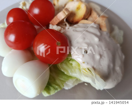 Caesar salad with crisp lettuce, cherry tomatoes, halved quail eggs, crunchy croutons and creamy dressing on a white plate - fresh, balanced lunch or light dinner choice 141945054