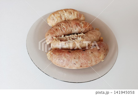 Cooked pork sausages with herbs and spices on a clear plate, offering a high-angle view of a tasty savory meal, ready for eating, isolated on a clean white background Cooked pork sausages with herbs and spices on a clear plate, offering a high-angle view of a tasty savory meal, ready for eating, isolated on a clean white background 141945058