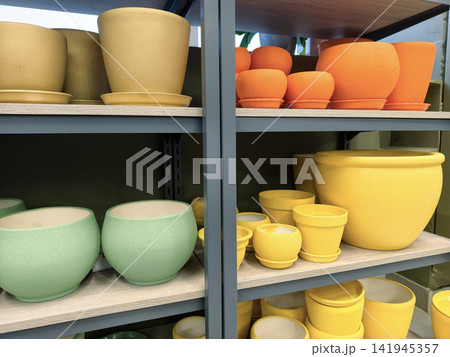 Golden, blue, orange and yellow ceramic flower pots with saucers in various sizes displayed on shelves in a retail garden section Golden, blue, orange and yellow ceramic flower pots with saucers in various sizes displayed on shelves in a retail garden section 141945357