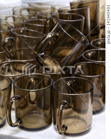Dark transparent glass cups displayed on supermarket shelves forming a simple modern kitchenware assortment designed for everyday use and retail sale in a grocery store 141945491