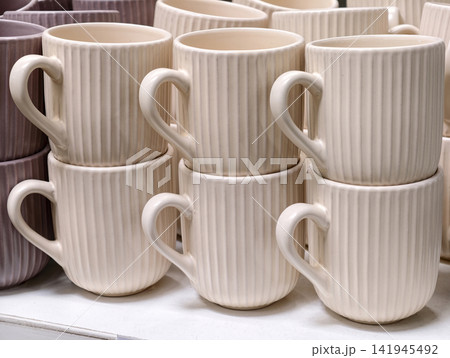 Ceramic cups arranged on retail shelves creating simple kitchenware set with functional design for everyday use and store display Ceramic cups arranged on retail shelves creating simple kitchenware set with functional design for everyday use and store display 141945492