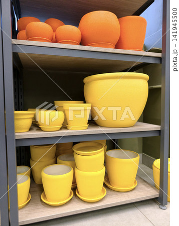 Yellow and red ceramic plant containers with saucers in large and small sizes arranged neatly on shelves in a home improvement store Yellow and red ceramic plant containers with saucers in large and small sizes arranged neatly on shelves in a home improvement store 141945500