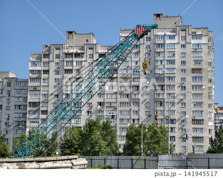 Construction site with large crane against residential building background highlighting structural development and modern urban expansion with industrial construction equipment Construction site with large crane against residential building background highlighting structural development and modern urban expansion with industrial construction equipment 141945517