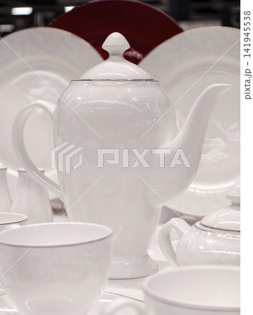White cups on saucers tall graceful porcelain teapot and plates behind forming elegant kitchenware set in refined retail display concept for luxury tableware marketing 141945538