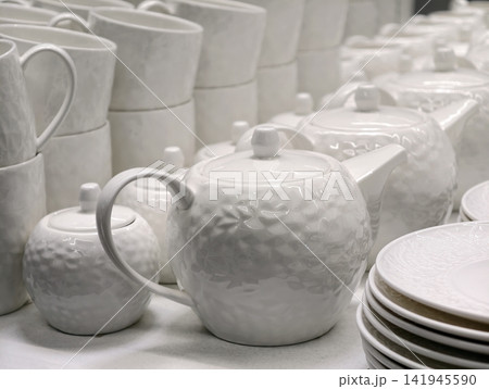 White porcelain mini teapots sugar bowls cups and plates forming basic kitchenware set in store shelf arrangement designed for practical everyday tableware use and retail sale 141945590
